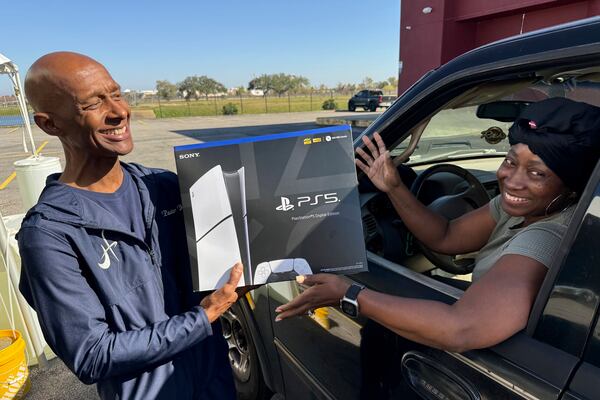 Pastor Antoine Barriere, left, hands a PlayStation 5 to Leticia Clanton after she handed over her handgun Tuesday, Dec. 31, 2024, in New Orleans. (AP Photo/Jack Brook)