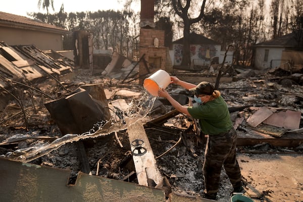 Nancy Belanger pours water on a neighbor's fire-ravaged property in the aftermath of the Palisades Fire in the Pacific Palisades neighborhood of Los Angeles, Thursday, Jan. 9, 2025. (AP Photo/Jae C. Hong)