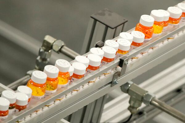 FILE- Bottles of medicine ride on a belt at a mail-in pharmacy warehouse in Florence, N.J., July 10, 2018. President Donald Trump’s plan to change the pricing model for some medications is facing fierce criticism from the pharmaceutical industry before he’s even signed an executive order he says will lower the costs of drugs. (AP Photo/Julio Cortez, File)