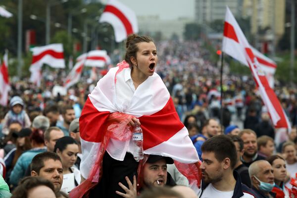 FILE - A woman covers herself with an old Belarusian national flag while shouting at police during a protest near the residence of President Alexander Lukashenko in Minsk, Belarus, Sept. 6, 2020. (AP Photo, File)