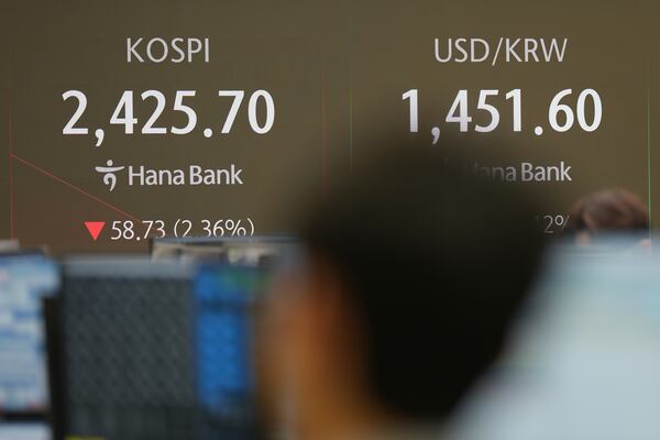 A currency trader walks by the screens showing the Korea Composite Stock Price Index (KOSPI), left, and the foreign exchange rate between U.S. dollar and South Korean won at a foreign exchange dealing room in Seoul, South Korea, Thursday, Dec. 19, 2024. (AP Photo/Lee Jin-man)