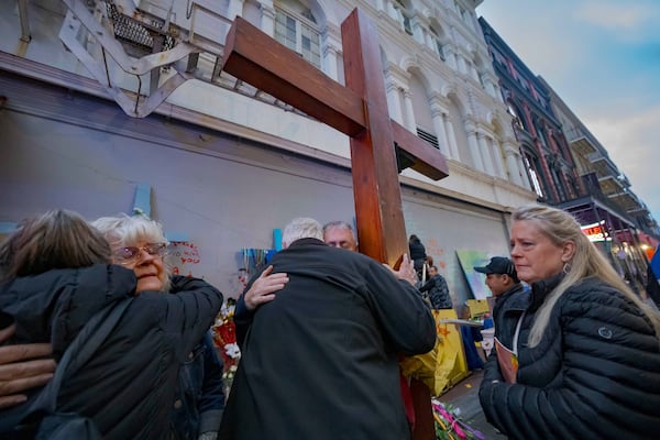 Long Island, N.Y. residents Cathy Tenedorio, second left, and Louis Tenedorio, center left, are hugged by supporters including Dan Beazley of Northville, Michigan, holding cross, as Linda Flick, right, looks toward a memorial on Bourbon Street and Canal Street in New Orleans, Saturday, Jan. 4, 2025, where Flick's nephew and the Tenedorio's son, Matthew Tenedorio, was killed in the New Year's Day attack. (AP Photo/Matthew Hinton)