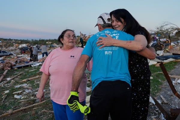 Bea Johnson, left, looks to her sister Kristie Sexton, right, as she is embraced by family friend Keith Adams as they stand next to Sexton's destroyed home after a severe storm passed through the area, Saturday, May 17, 2025, in London, Ky. (AP Photo/Carolyn Kaster)