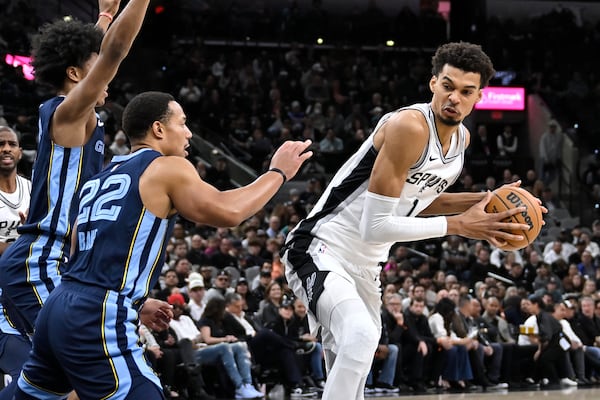 San Antonio Spurs' Victor Wembanyama (1) drives against Memphis Grizzlies' Desmond Bane (22) and Jaylen Wells during the first half of an NBA basketball game, Friday, Jan. 17, 2025, in San Antonio. (AP Photo/Darren Abate)