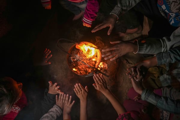 Reda Abu Zarada, 50, displaced from Jabaliya in northern Gaza, warms up by a fire with her grandchildren at a camp in Khan Younis, Gaza Strip, Thursday, Dec. 19, 2024. (AP Photo/Abdel Kareem Hana)