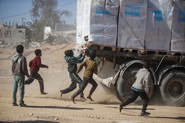 Palestinians chase humanitarian aid trucks that arrived through the Kerem Shalom crossing from Egypt into the Gaza Strip, in Rafah, Tuesday, Jan. 21, 2025. (AP Photo/Jehad Alshrafi)