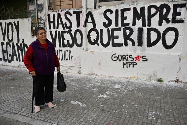 A woman watches the funeral procession of former President Jose Mujica from the presidential palace to the National Assembly, next to graffiti that reads in Spanish: "Farewell dear old man," in Montevideo, Uruguay, Wednesday, May 14, 2025. (AP Photo/Santiago Mazzarovich)