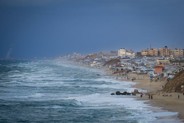 People walk along the beach next to a tent refugee camp for displaced Palestinians in Deir al-Balah, central Gaza Strip, Monday, Dec .30, 2024. (AP Photo/Abdel Kareem Hana)