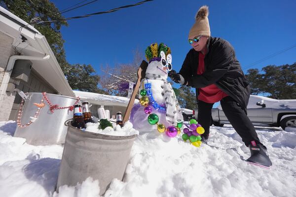 Stacy Centanni refreshes their, Mardi Gras festooned snowman as it melts in the sun, the day after a rare and record setting snowstorm in River Ridge, La., a suburb of New Orleans, Wednesday, Jan. 22, 2025. (AP Photo/Gerald Herbert)