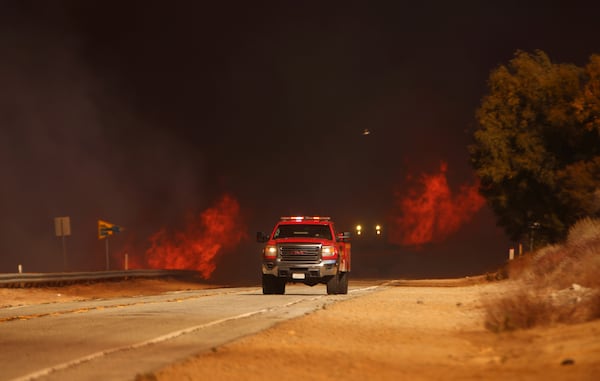 A fire truck drives past flames caused by the Hughes Fire in Castaic, Calf., Wednesday, Jan. 22, 2025. (AP Photo/Ethan Swope)