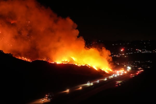 Vehicles drive along Interstate 15 as the Lilac Fire burns along a hillside in Bonsall, Calif., Tuesday, Jan. 21, 2025. (AP Photo/Jae C. Hong)