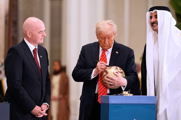 President Donald Trump signs a FIFA soccer ball as Qatar's Emir Sheikh Tamim bin Hamad Al Thani and FIFA President Gianni Infantino looks on at the Lusail Palace, Wednesday, May 14, 2025, in Doha, Qatar, as they marked the passing of World Cup hosting duties from Qatar, which held it in 2022, to the United States, which is hosting in 2026. (AP Photo/Alex Brandon)