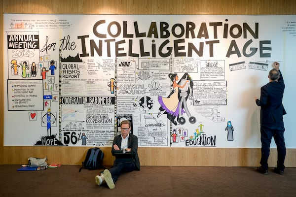 A man paints on a large poster at the Annual Meeting of World Economic Forum in Davos, Switzerland, Wednesday, Jan. 22, 2025. (AP Photo/Markus Schreiber)