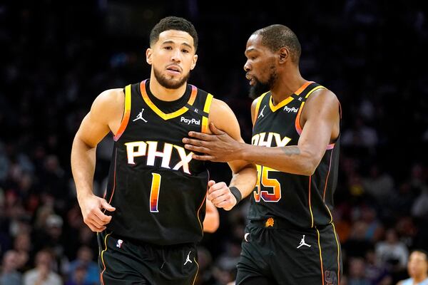 Phoenix Suns guard Devin Booker (1) gets a pat on the chest from Kevin Durant (35) during the first half of an NBA basketball game against the Memphis Grizzlies Tuesday, Dec. 31, 2024, in Phoenix. (AP Photo/Darryl Webb)