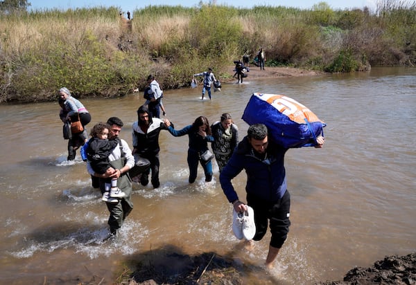 Syrian families who fled the clashes in Syria hold their luggages as they cross a river marking the border between Syria and northern Lebanon in Heker al-Daher village in Akkar province, Tuesday, March 11, 2025. (AP Photo/Hussein Malla)