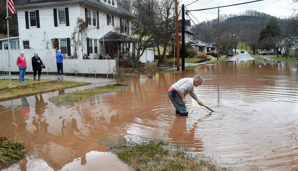 Harry Miller works to open a clogged sewer drain near his house in Nitro, W.Va., as his neighbors look on Thursday, Feb. 6, 2025. (Chris Dorst/Charleston Gazette-Mail via AP)