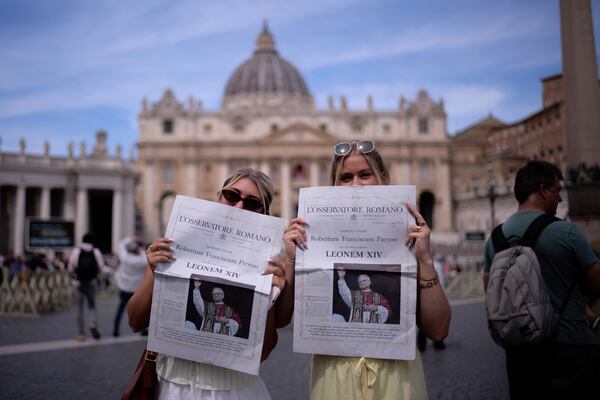 Mackenzie Magas and Kaylee Mellentine from Missouri, pose for a photo with a newspaper showing the new Pope Leo XIV on the front page, in front of the St. Peter Basilica at the Vatican, Friday, May 9, 2025. (AP Photo/Markus Schreiber)