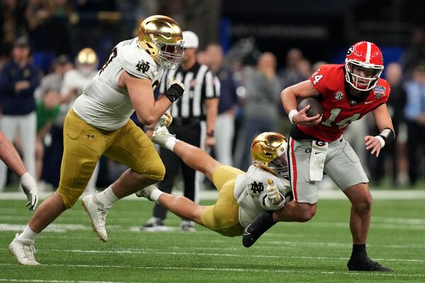 Georgia quarterback Gunner Stockton (14) runs from Notre Dame linebacker Drayk Bowen, center, and defensive lineman Gabriel Rubio, left, during the first half in the quarterfinals of a College Football Playoff, Thursday, Jan. 2, 2025, in New Orleans. (AP Photo/Gerald Herbert)