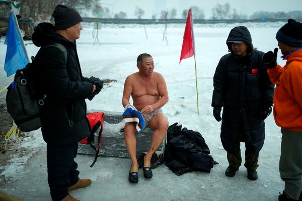 A man chats with residents in winter clothings as he prepares to swim in a pool carved from ice on the frozen Songhua river in Harbin in northeastern China's Heilongjiang province, Tuesday, Jan. 7, 2025. (AP Photo/Andy Wong)