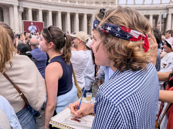Notre Dame's architecture college student Wesley Buonerba, wearing a us flag bandanna, does a watercolor sketch of the loggia of St. Peter's Basilica during Pope Leo XIV first Sunday blessing of faithful gathered in the square for the traditional blessing, Sunday, May 11, 2025. (AP Photo/Giovanna Dell'Orto)