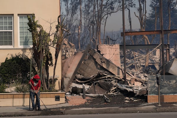 A person begins cleaning up after the Palisades Fire ravaged a neighborhood amid high winds in the Pacific Palisades neighborhood of Los Angeles, Wednesday, Jan. 8, 2025. (AP Photo/Damian Dovarganes)