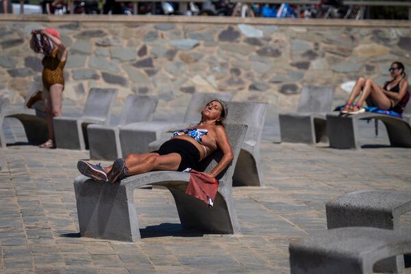 FILE - People sunbathe on a promenade in Barcelona, Spain, Wednesday, July 24, 2024. Several regions of Spain are under alert for high temperatures. (AP Photo/Emilio Morenatti,File)