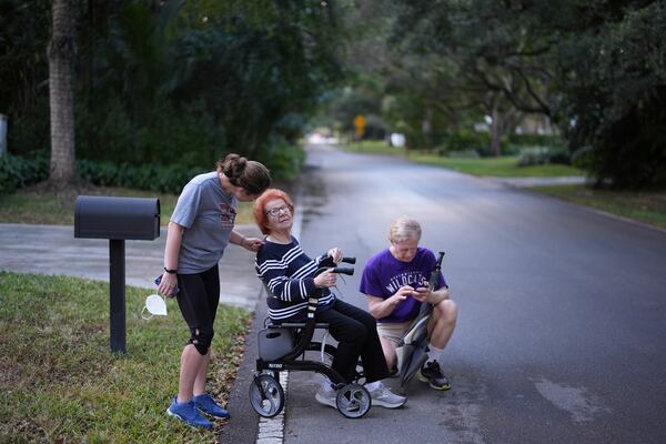 Kira Levin, 29, left, talks with grandmother Jeanette Levin, 98, during a break in Jeanette's daily walk with her granddaughter and her son, Eliot Levin, right, in Pinecrest, Fla., Monday, Dec. 16, 2024. (AP Photo/Rebecca Blackwell)