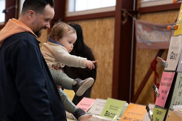 Aaron Swindle and his daughter Zoe look at product price signs at the Brighton Farmers Market on Sunday, March 23, 2025, in Brighton, N.Y. (Caitlyn Daproza via AP)
