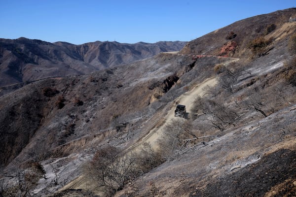 A vehicle is driven through a burned mountain road in the aftermath of the Palisades Fire in Mandeville Canyon Tuesday, Jan. 14, 2025, in Los Angeles. (AP Photo/Ethan Swope)