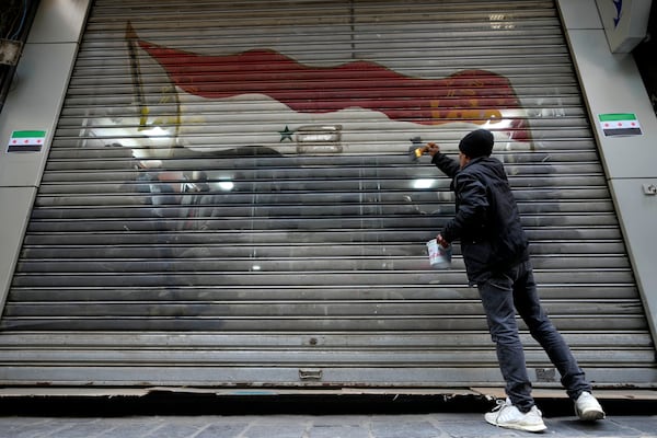 A worker removes from a door shop the colours of the official flag of the ousted government, in Damascus, Syria, Friday, Dec. 20, 2024. (AP Photo/Hussein Malla)