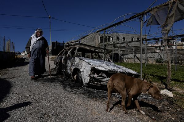 A Palestinian stands beside a torched car in the aftermath of an attack by Israeli settlers in the West Bank village of Jinsafut, Tuesday, Jan. 21, 2025. (AP Photo/Majdi Mohammed)