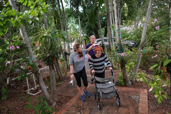 Kira Levin, 29, left, holds a hand over the hair of her grandmother Jeanette Levin, as it begins to rain at the end of Jeanette's daily walk with her granddaughter and her son, Eliot Levin, back, in Pinecrest, Fla., Monday, Dec. 16, 2024. (AP Photo/Rebecca Blackwell)