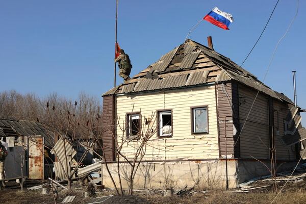 In this photo taken from video distributed by Russian Defense Ministry Press Service on Friday, March 14, 2025, a Russian soldier rises a red flag atop of a house at an area in the Kursk region of Russia after it was taken over by Russian troops. (Russian Defense Ministry Press Service via AP)