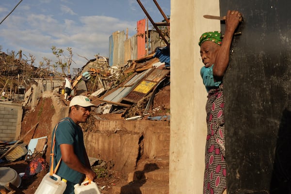 People walk past debris in the Kaweni slum Thursday, Dec. 19, 2024, on the outskirts of Mamoudzou, in the French Indian Ocean island of Mayotte, after Cyclone Chido. (AP Photo/Adrienne Surprenant)