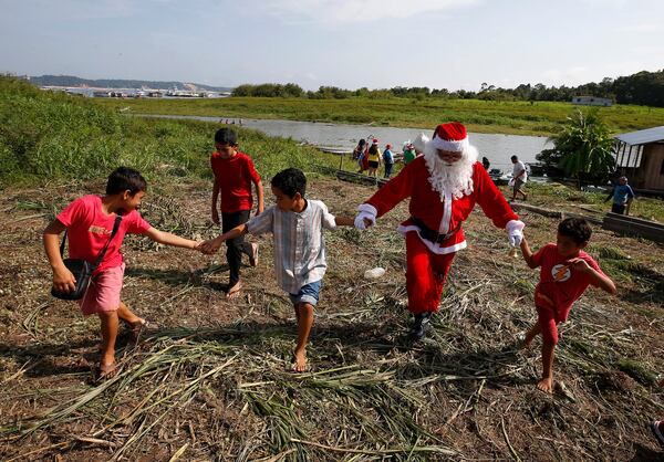 Jorge Barroso, dressed as Santa Claus, is received by young residents after arriving on a boat to distribute Christmas gifts to children who live in the riverside communities of the Amazon, in Iranduba, Brazil, Saturday, Dec. 21, 2024. (AP Photo/Edmar Barros)