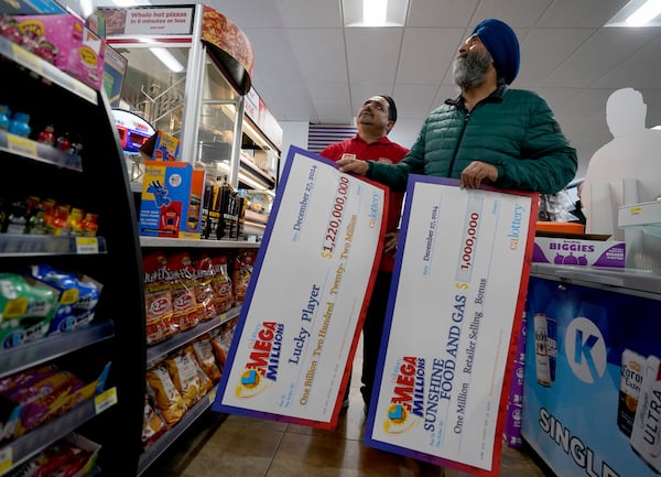 Jaspal Singh, right, and store employee Bob Singh, left, look for a spot to place two enlarged images of lottery payoff checks, at the family store, Saturday, Dec. 28, 2024, where the winning lotto ticket was purchased in Cottonwood, Calif. (AP Photo/Rich Pedroncelli).