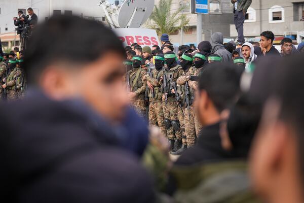 Palestinians watch as Hamas fighters stand in formation ahead of the hand over to the Red Cross of three Israeli hostages as part of the Gaza ceasefire deal with Israel in Deir Al-Balah, central Gaza Strip, Saturday Feb. 8, 2025.(AP Photo/Abdel Kareem Hana)