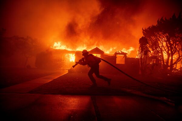 FILE - A firefighter battles the Palisades Fire as it burns a structure in the Pacific Palisades neighborhood of Los Angeles, Jan. 7, 2025. (AP Photo/Ethan Swope,File)