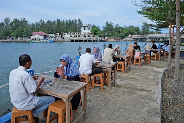 People sit at a cafe on the waterfront near Ulhee Lheue beach, one of the areas hardest his by the Indian Ocean tsunami in 2004, in Banda Aceh, Indonesia, Saturday, Dec 14, 2024. (AP Photo/Achmad Ibrahim)