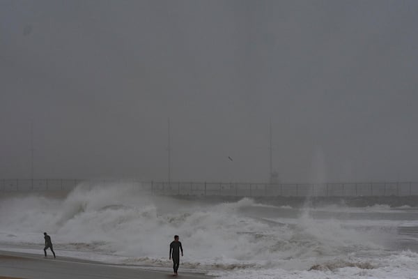 Two surfers walk along the beach as waves crash in Seal Beach, Calif., Tuesday, Dec. 24, 2024. (AP Photo/Jae C. Hong)