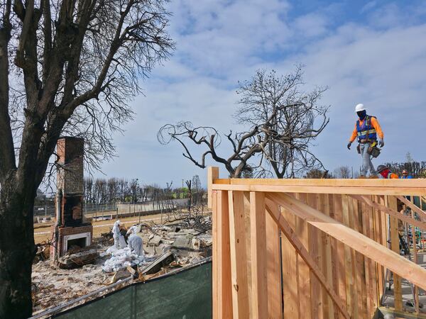 A worker stands atop a home being rebuilt after the Palisades Fire in the Pacific Palisades neighborhood of Los Angeles, Thursday, April 24, 2025. (AP Photo/Damian Dovarganes)