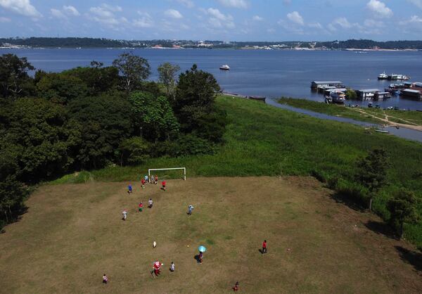 Jorge Barroso, dressed as Santa Claus, joins young residents in a pick up soccer game after arriving on a boat to distribute Christmas gifts to the children, in Iranduba, Brazil, Saturday, Dec. 21, 2024. (AP Photo/Edmar Barros)