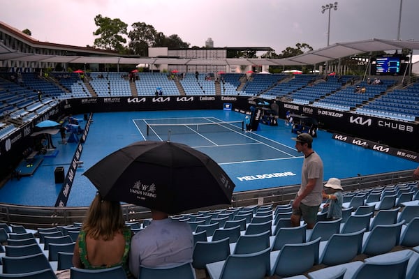 Spectators wait under umbrellas as rain suspends play during first round matches at the Australian Open tennis championship in Melbourne, Australia, Sunday, Jan. 12, 2025.(AP Photo/Manish Swarup)