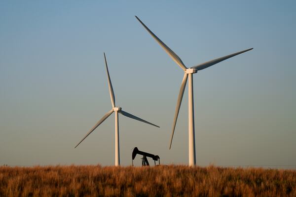 FILE - An oil pumping unit works in the foreground while wind turbines at the Buckeye Wind Energy wind farm rise in the distance Sept. 30, 2024, near Hays, Kan. (AP Photo/Charlie Riedel, File)