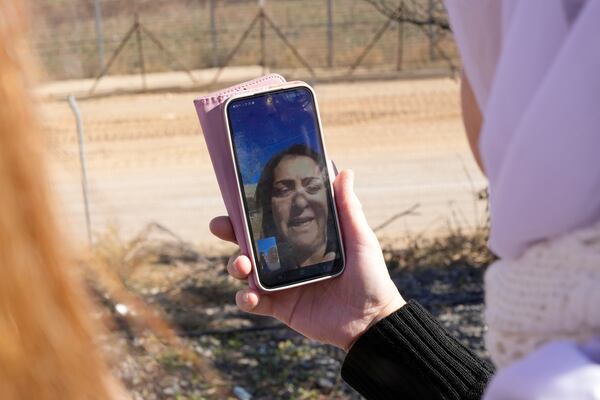 Samar Safadi holds her phone as she talks by video call with her sister, Sawsan, who lives inside the buffer zone near the "Alpha Line" that separates the Israeli-controlled Golan Heights from Syria, in the town of Majdal Shams, Wednesday, Dec. 18, 2024. (AP Photo/Matias Delacroix)