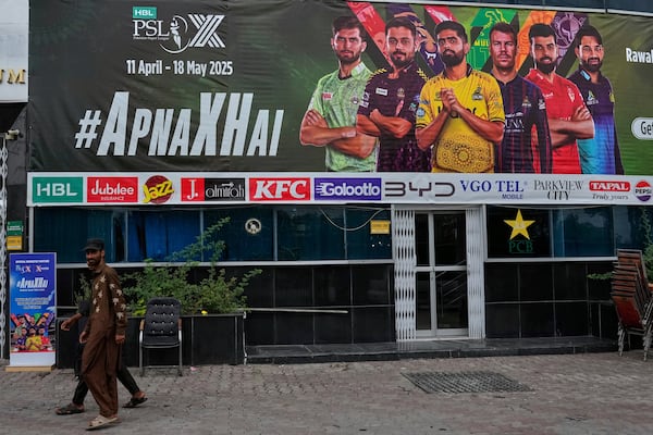 Workers walk past an advertisement board of Pakistan Super League Twenty20 tournament with the pictures of cricketers, installed at the Rawalpindi Cricket Stadium, in Rawalpindi, Pakistan, Friday, May 9, 2025. (AP Photo/Anjum Naveed)