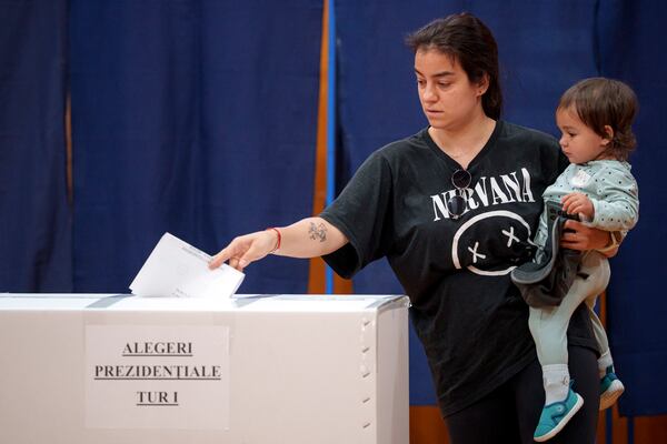 A woman holds a baby as she casts her vote in the first round of the presidential election redo in Bucharest, Romania, Sunday, May 4, 2025. (AP Photo/Andreea Alexandru)