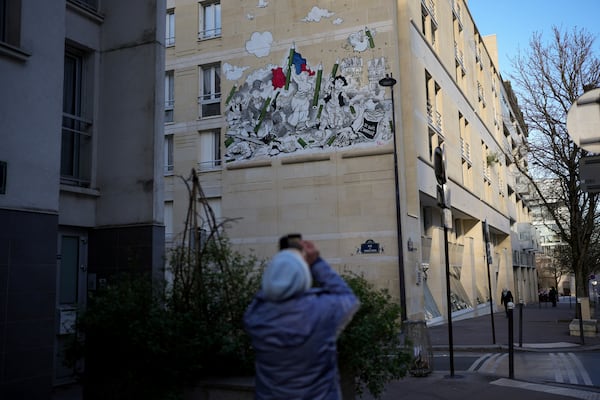 A woman takes a snapshot of a fresco by French street artist Nilko referring to the "Liberty Leading the People" painting by Eugene Delacroix during commemorations marking 10 years since an Islamist attack on the Charlie Hebdo satirical newspaper and the Hypercacher jewish supermarket, in Paris Tuesday Jan. 7, 2025. (AP Photo/Thibault Camus)