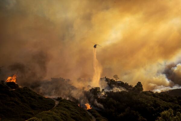 Water is dropped on the advancing Palisades Fire by helicopter in the Pacific Palisades neighborhood of Los Angeles, Tuesday, Jan. 7, 2025. (AP Photo/Ethan Swope)