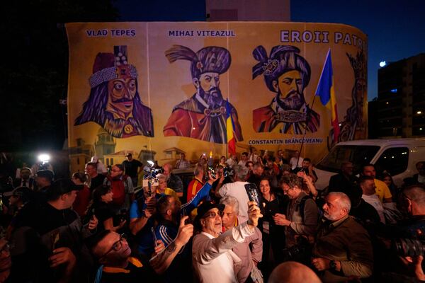 Supporters of presidential candidate George Simion react to the exit poll results, backdropped by depictions of Romanian historical figures, outside the headquarters of the Alliance for the Unity of Romanians (AUR) after polls closed for the first round of the country's presidential election redo in Bucharest, Romania, Sunday, May 4, 2025. (AP Photo/Andreea Alexandru)